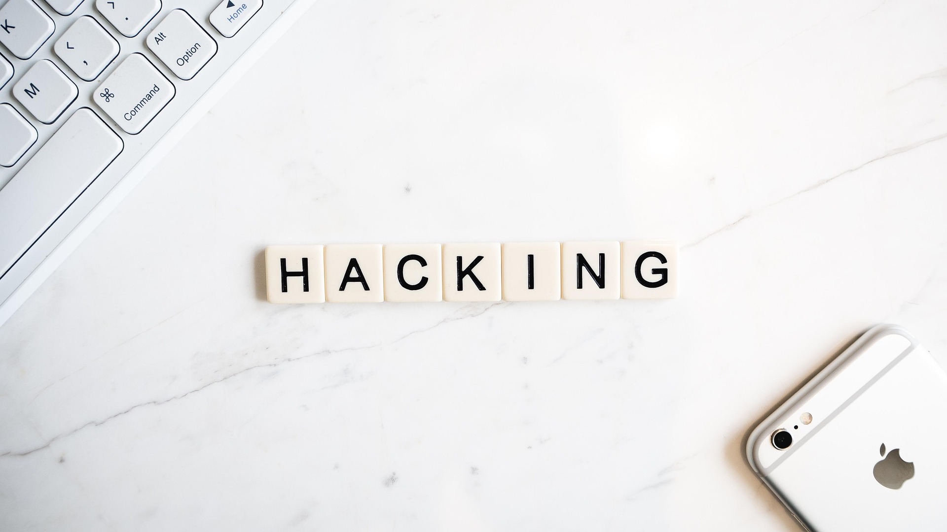 Lettres de Scrabble formant "HACKING" entre clavier et smartphone.